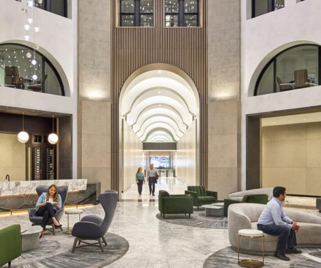 An office lobby concept with high ceilings. Two people sit on chairs while two others walk in from the hallway.