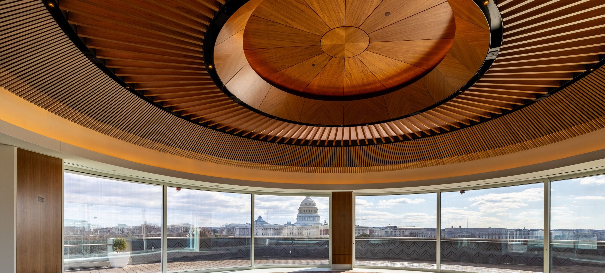 A wood ceiling with circular slatting surrounding a medallion at the center. The windows of the room look out over the Washington, D.C. Capitol
